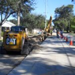 An excavator and other equipment install a pipeline on a residential road