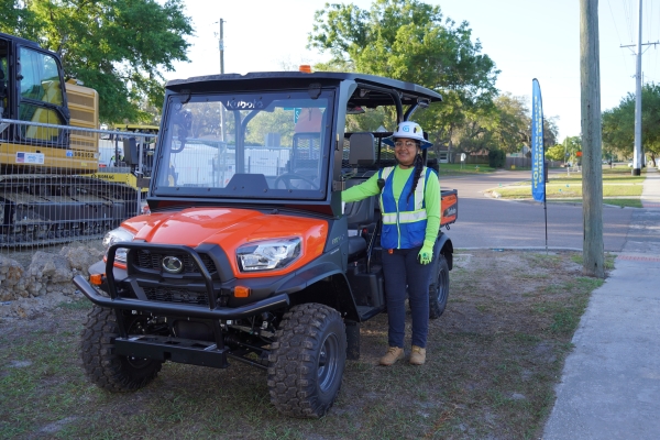 A community coordinator is shown wearing a blue vest standing next to an all-terrain vehicle that is used to transport residents as needed.